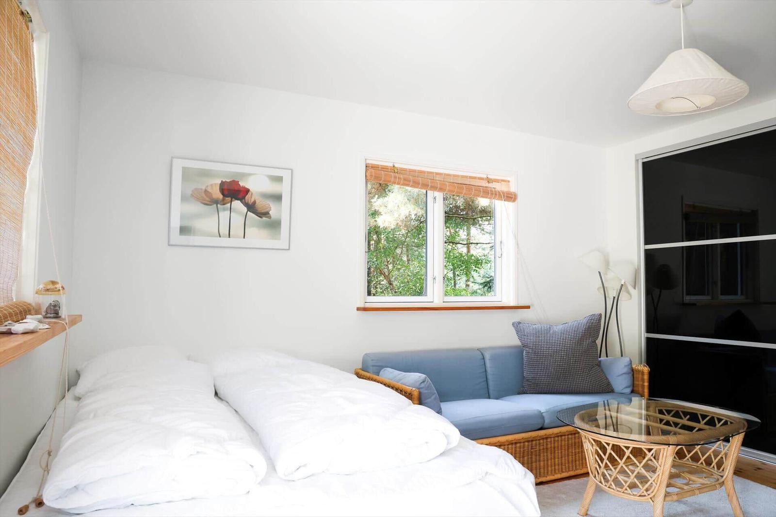 Schlafzimmer mit Bett, Sofa und Fenster mit Blick auf Wald.