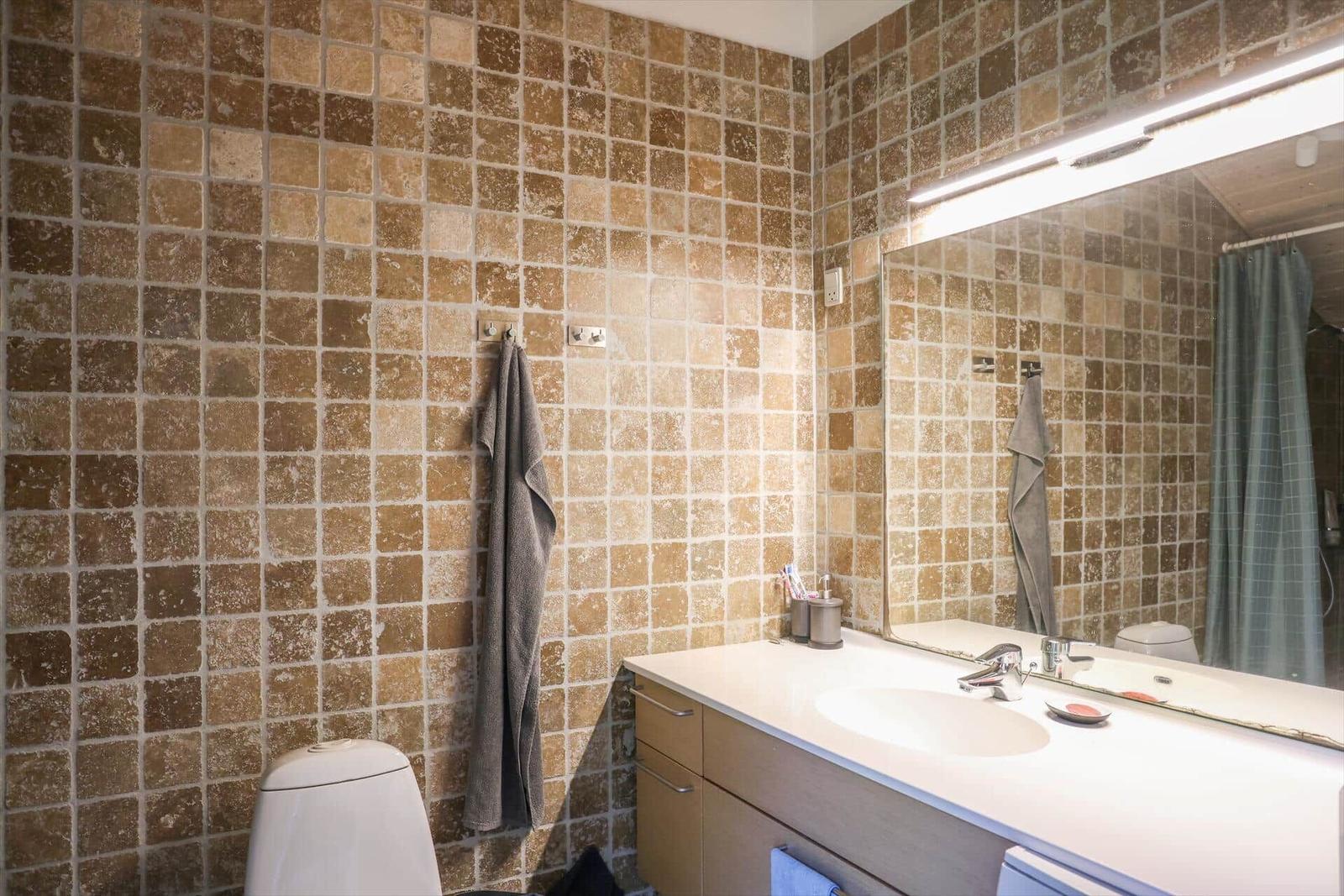 Badezimmer mit braunen Fliesen, Waschtisch und Spiegel.