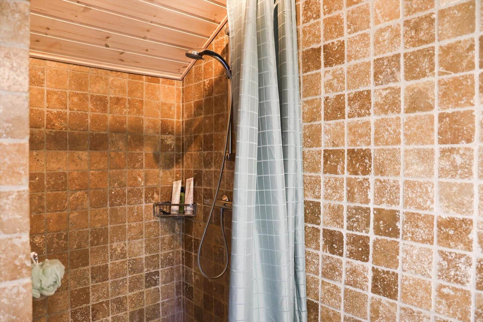 Dusche mit braunen Fliesen, Holzdecke und grauem Duschvorhang.