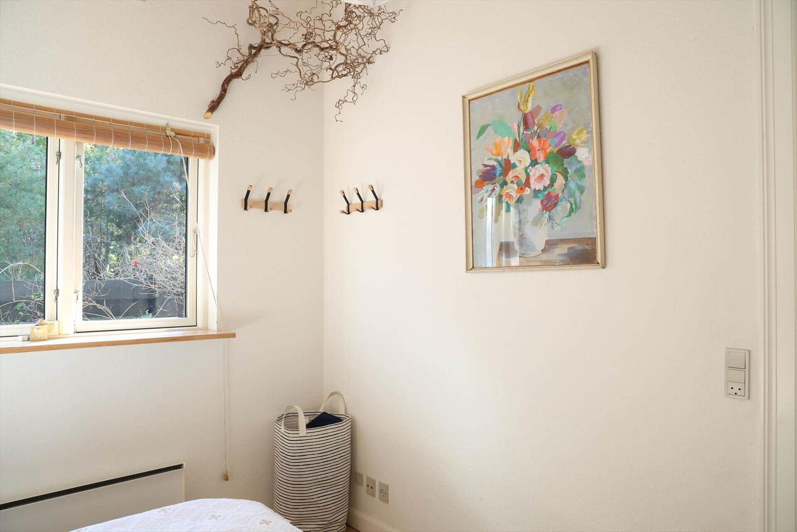Ein Raum mit Fenster, Wandbild und Haken. Ein gestreifter Korb steht im Ecke.
