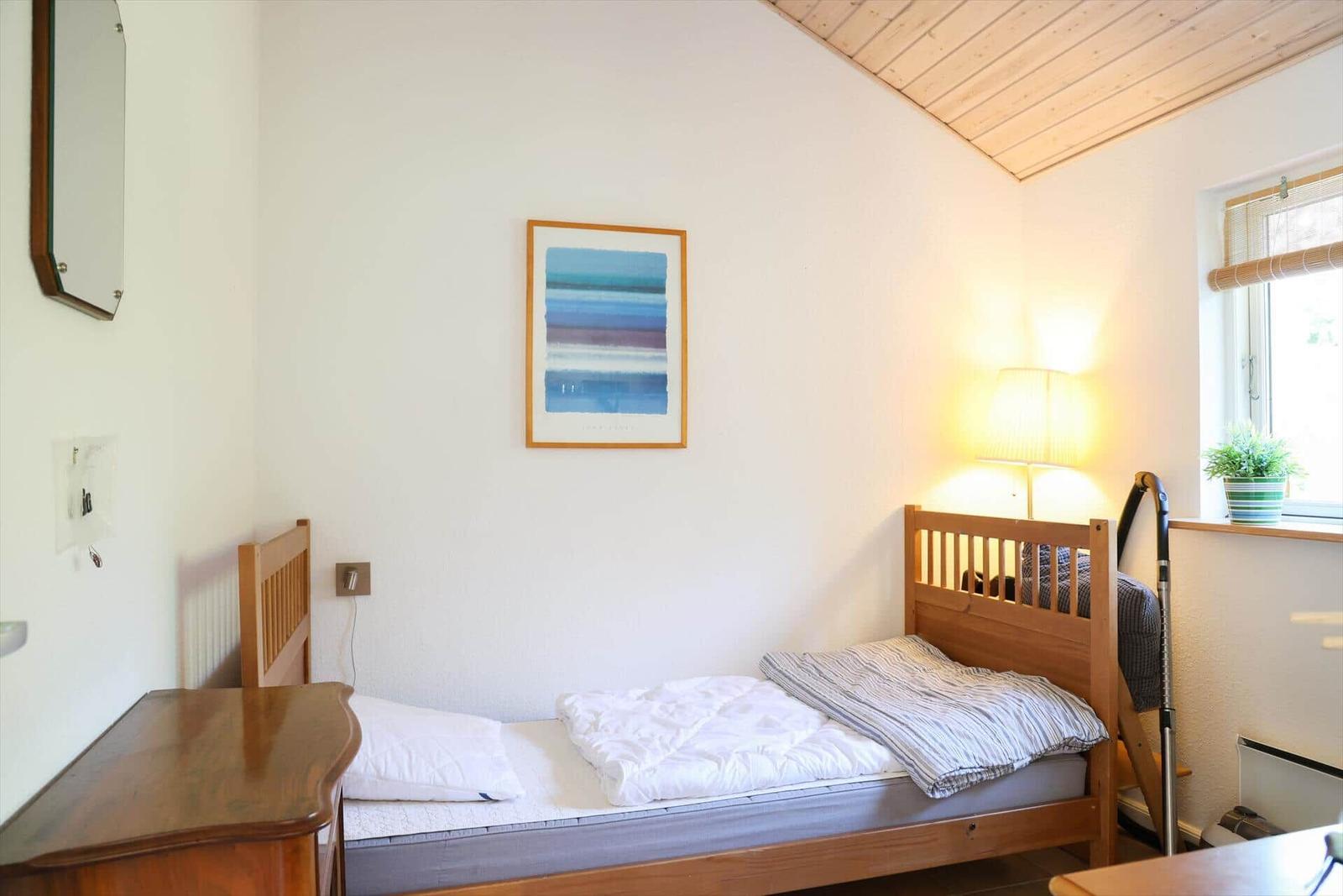 Ein Schlafzimmer mit Holzbett, Wandbild und Fenster mit Pflanze.
