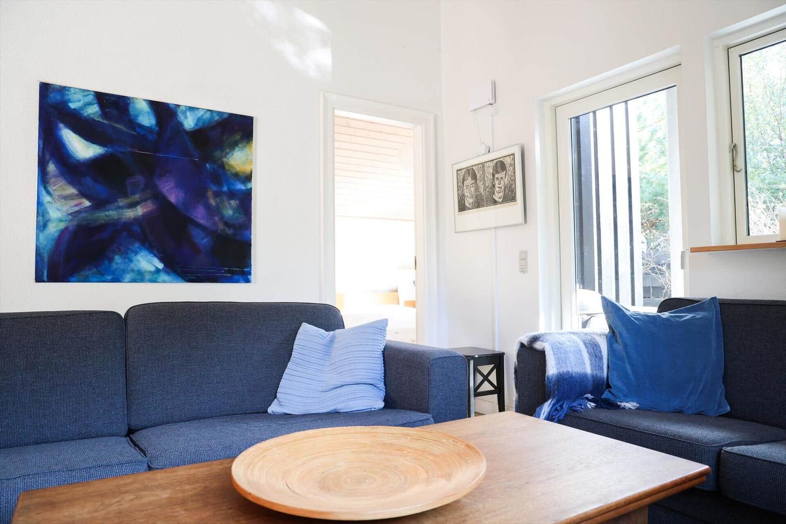 Ein Wohnzimmer mit blauem Sofa, Holztisch und Wandbildern.