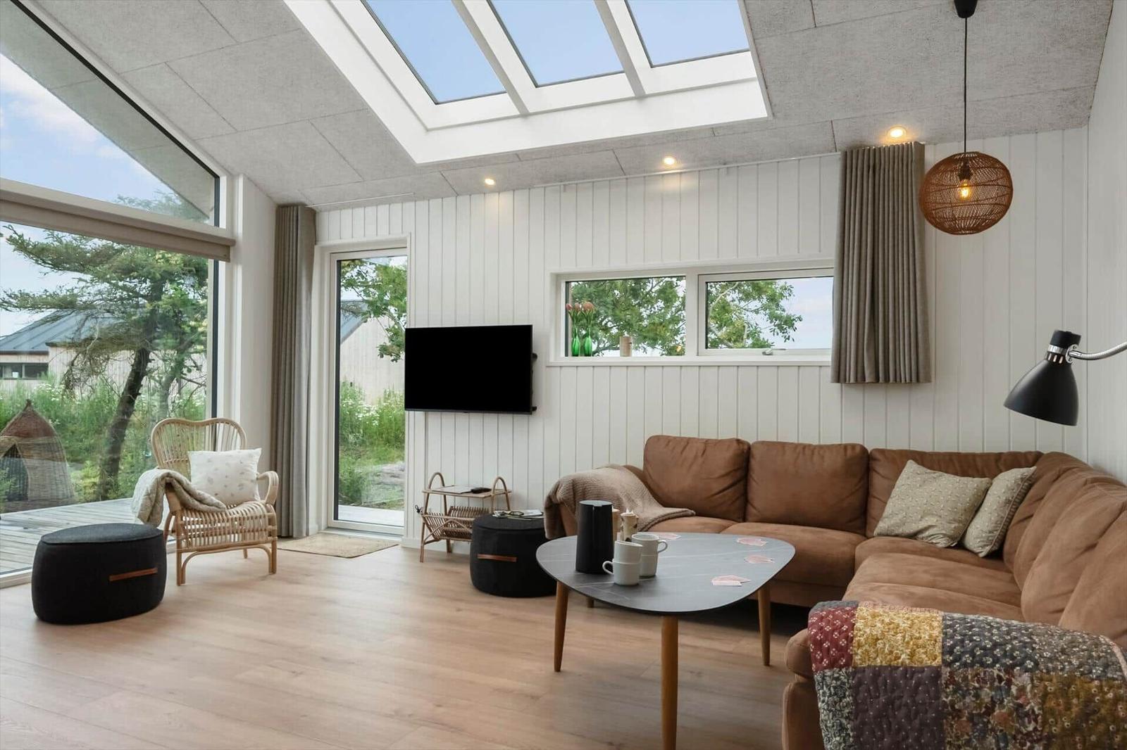 Wohnzimmer mit braunem Sofa, runden Tisch und großen Fenstern. Deckenfenster und Holzboden.