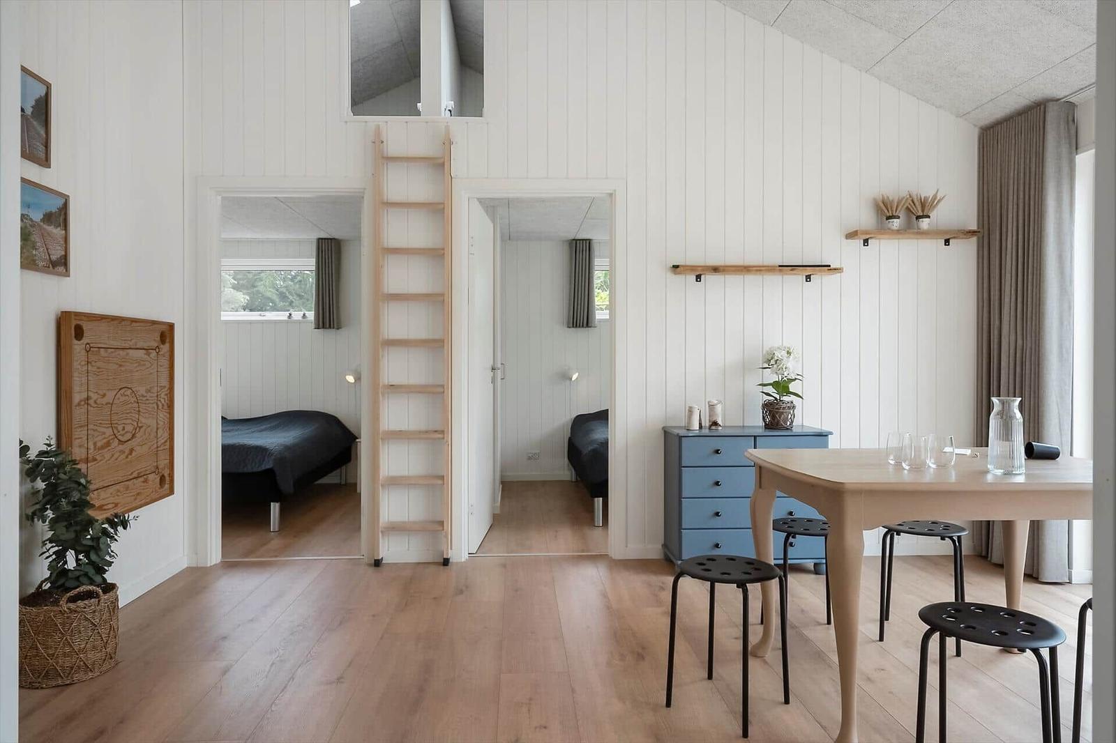 Wohnraum mit Treppe, Schlafzimmer und Esstisch. Holzdielen und weiße Wände.