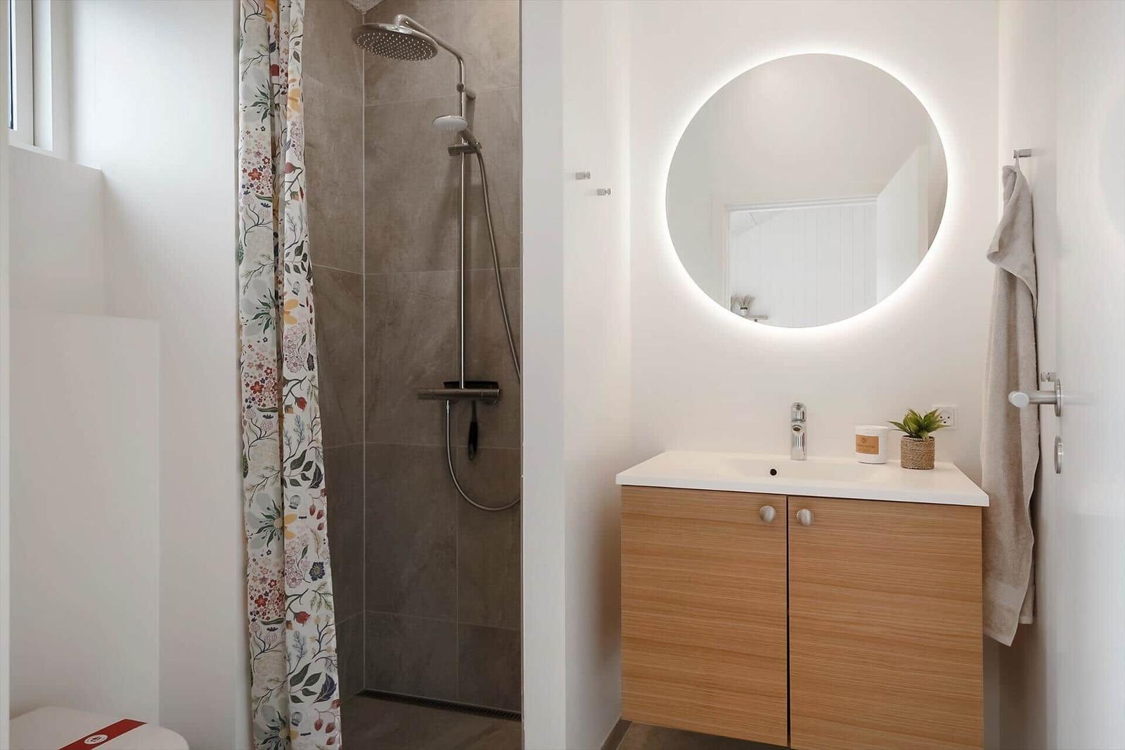 Dusche mit floraler Gardine und Waschbecken mit runden Spiegel.