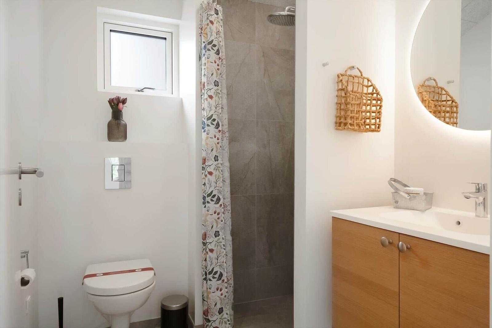 Badezimmer mit Dusche, Waschbecken und Toilette. Wandspiegel und Korb sind sichtbar.