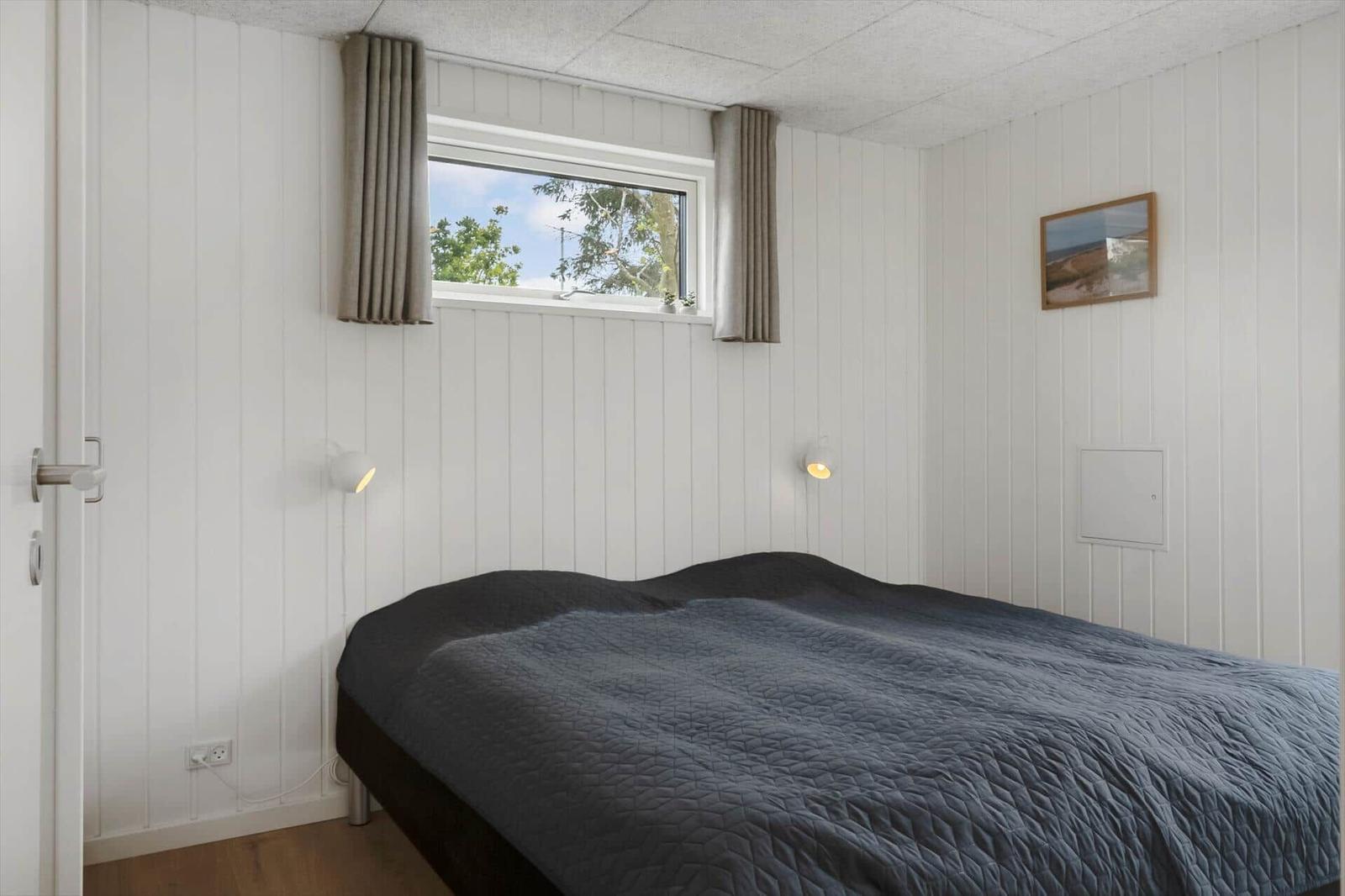 Schlafzimmer mit Bett, Fenster und weißen Wänden.