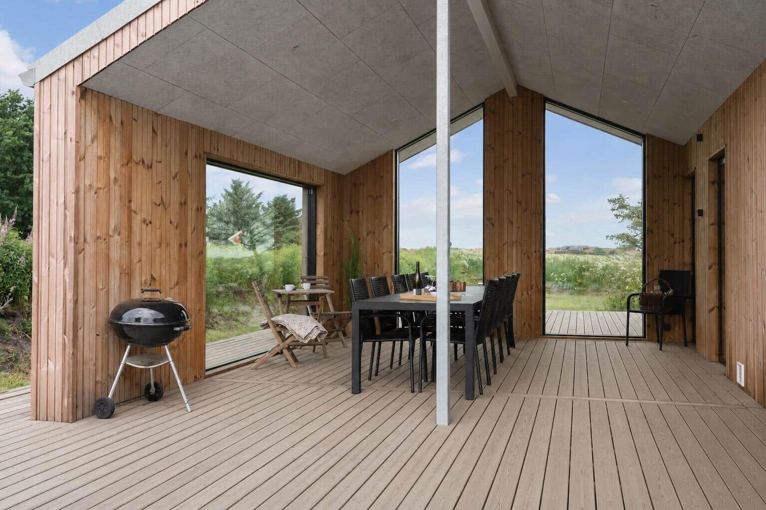 Terrasse mit Esstisch, Grill und großzügigen Fenstern zur Landschaft.