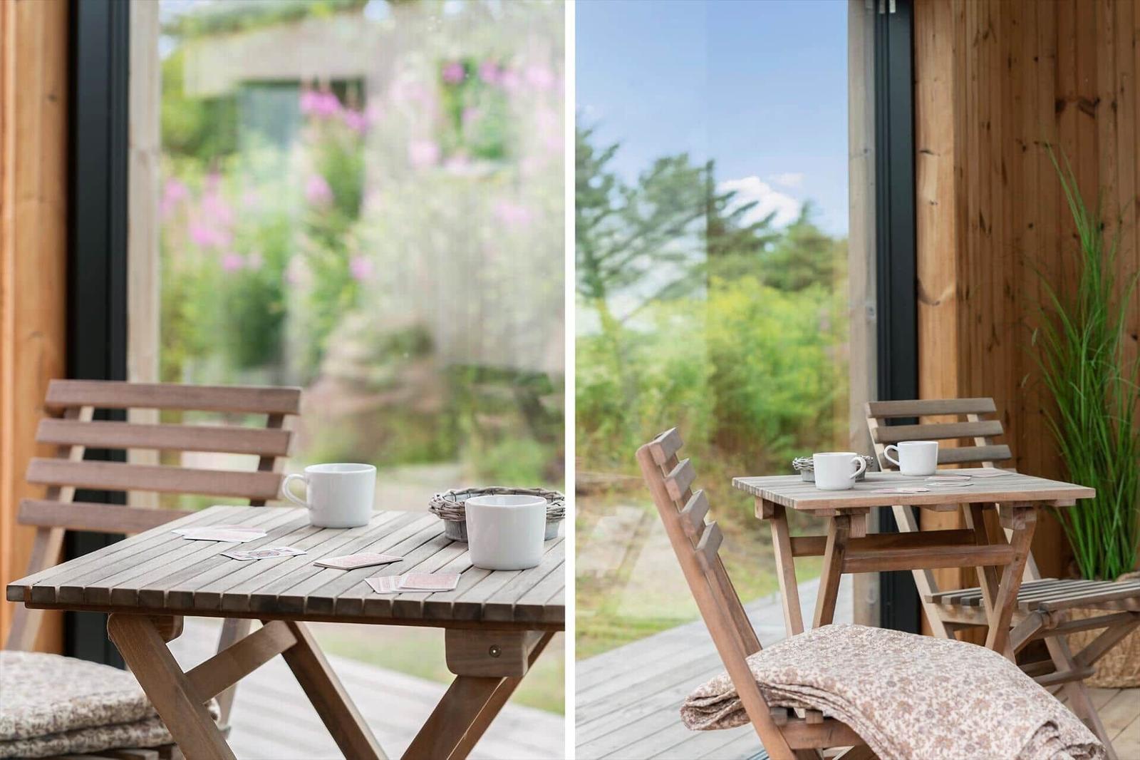 Holztisch mit zwei Stühlen und Tassen auf Terrasse mit Blick auf Garten.