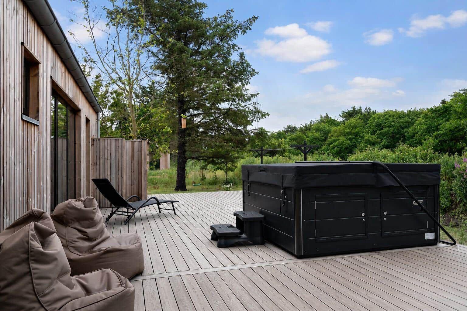 Terrasse mit Whirlpool, Liegestühlen und Beistühlen. Hintergrund: Wald und blauer Himmel.