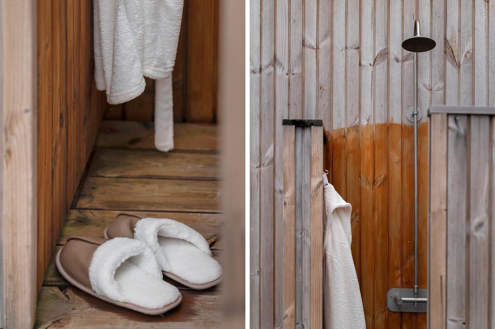 Holzverkleidete Dusche mit Duschbrause und Handtuch. Weiße Frottierbademantel und Hausschuhe auf Holzboden.