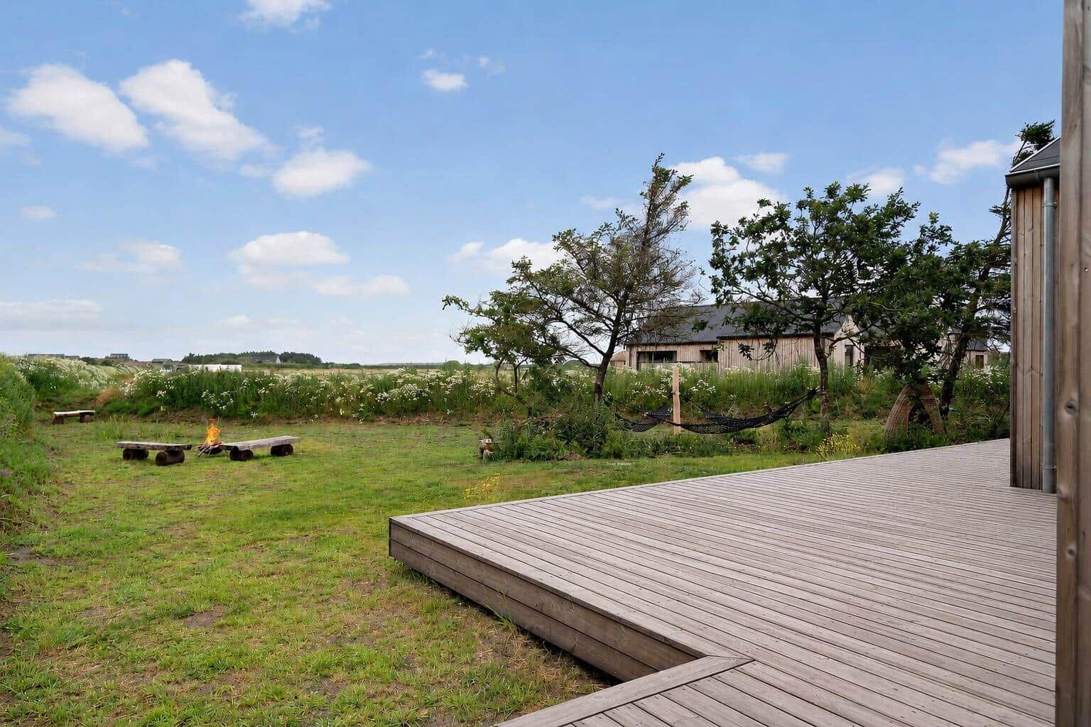 Holzterrasse mit Blick auf Grasland, Bäume und Ferienhaus im Hintergrund.