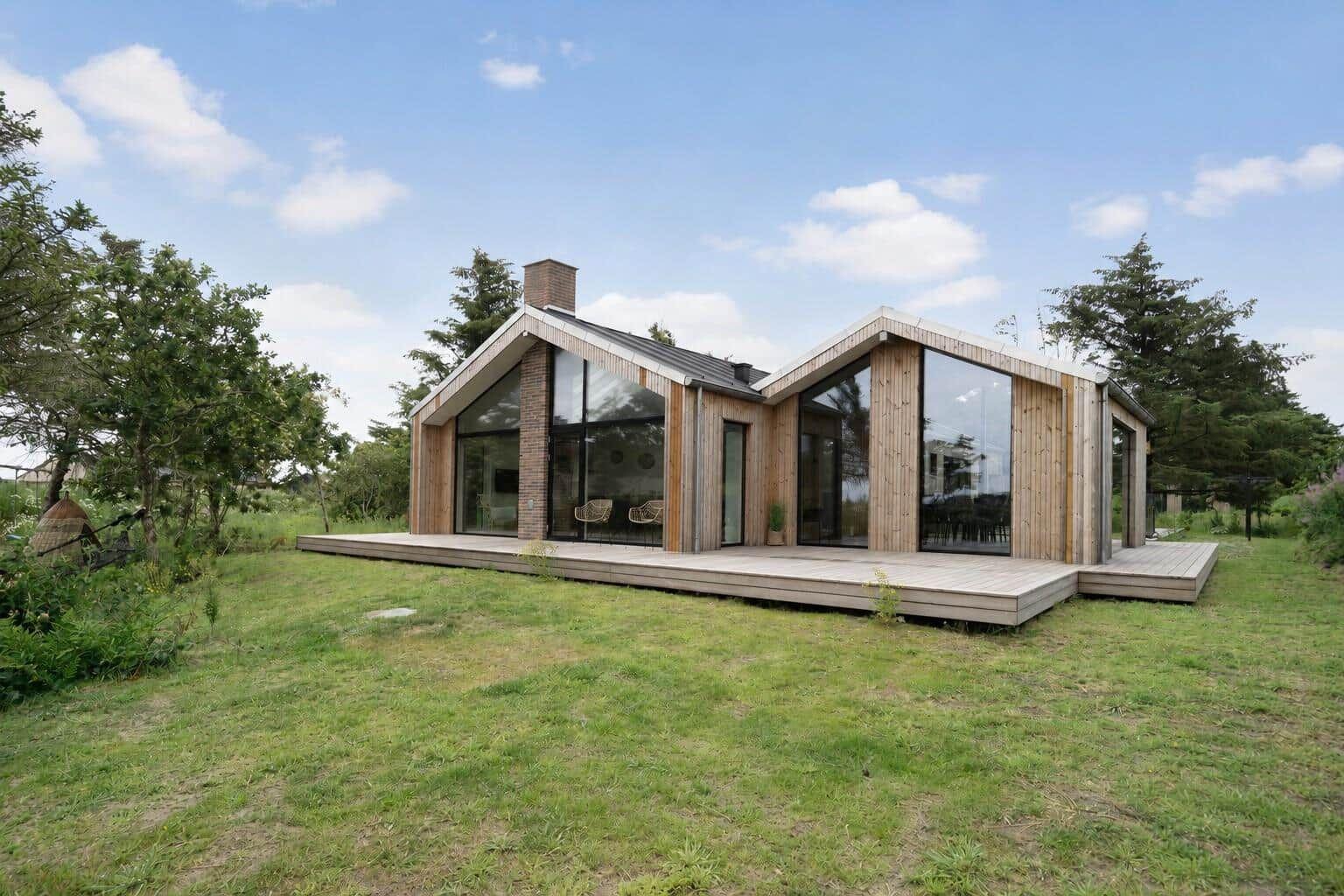 Moderne Holzhütte mit großem Terrassenbereich und Glasfassade im Grünen.