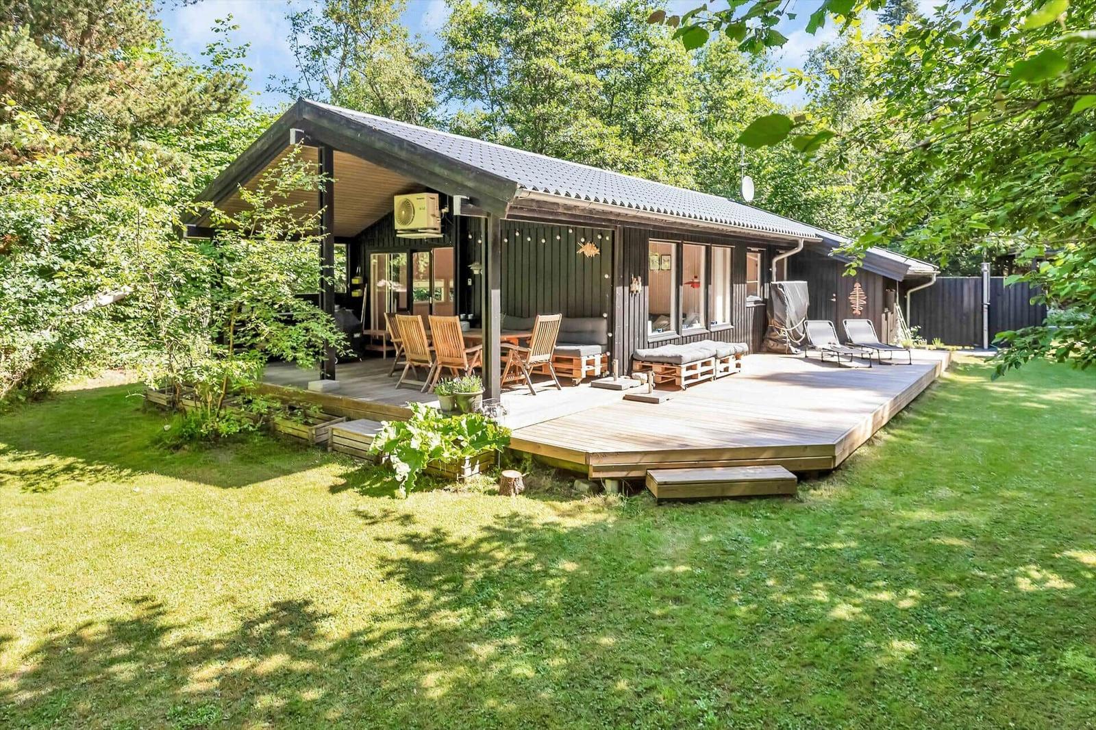Haus mit Holzterrasse, Garten und Sitzgelegenheiten im Grünen.