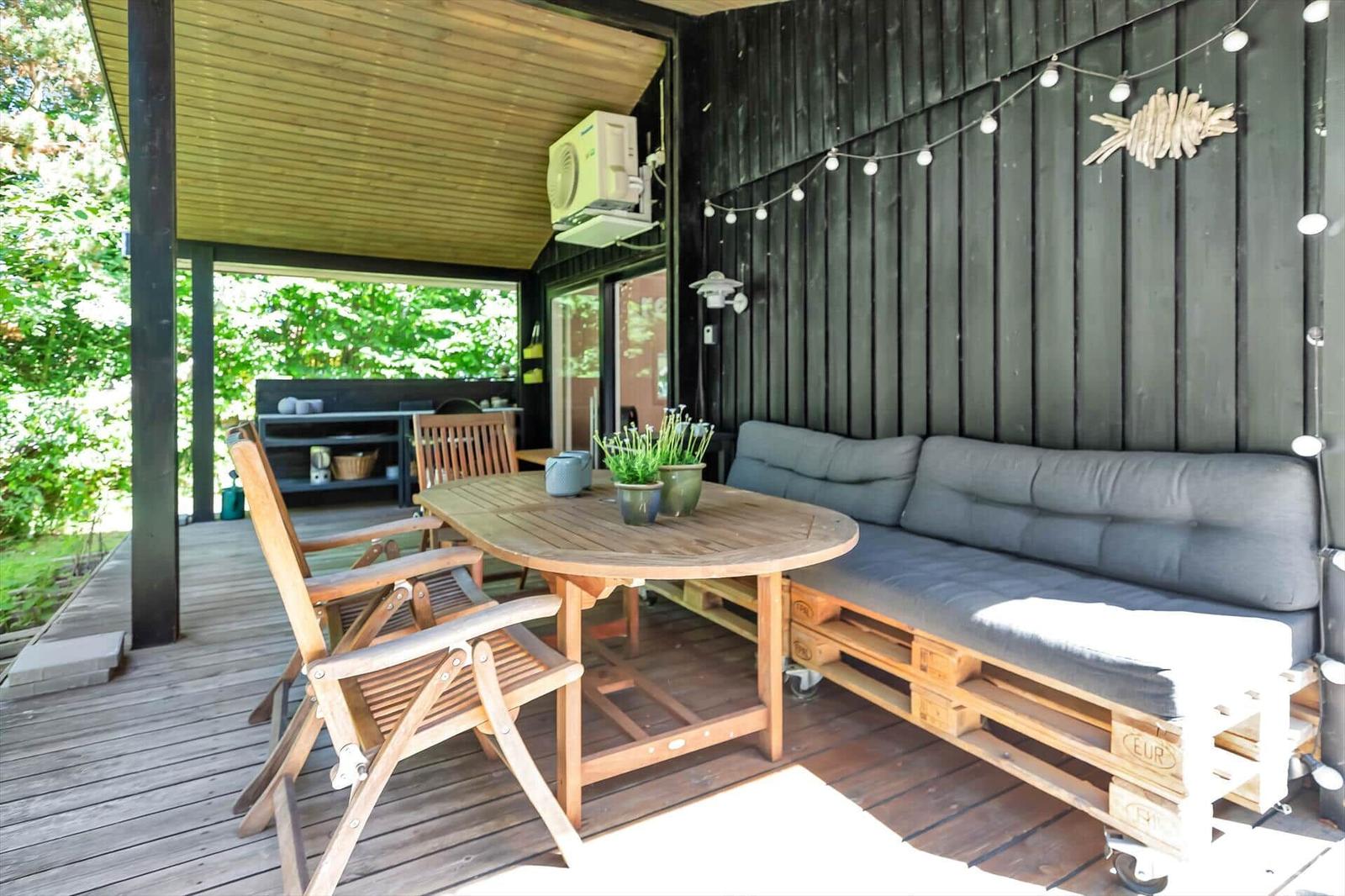 Terrasse mit Holztisch, Stühlen und Sofa aus Paletten. Hintergrund: Grillbereich und Wald.