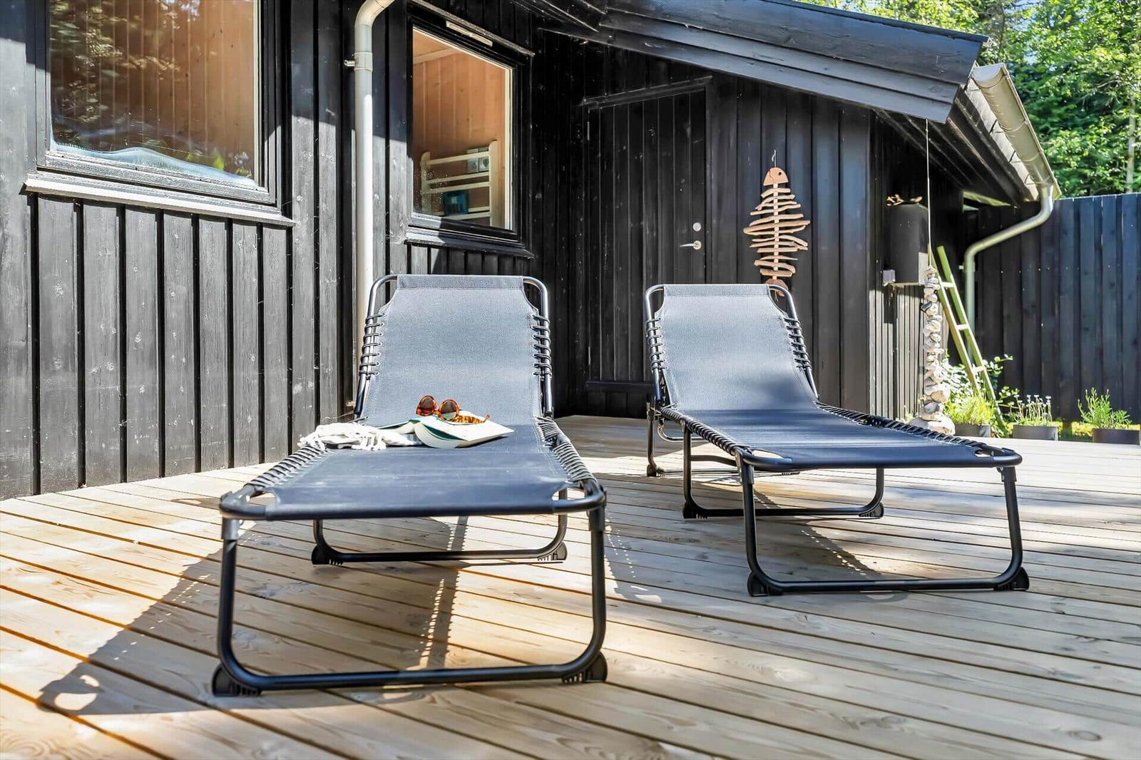Zwei Liegestühle auf einer Holterrasse vor einem dunklen Holzhaus.