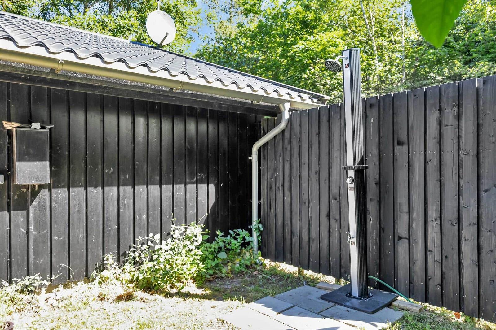 Außen-Dusche neben schwarzem Holzzaun und Gebäude mit Dach.