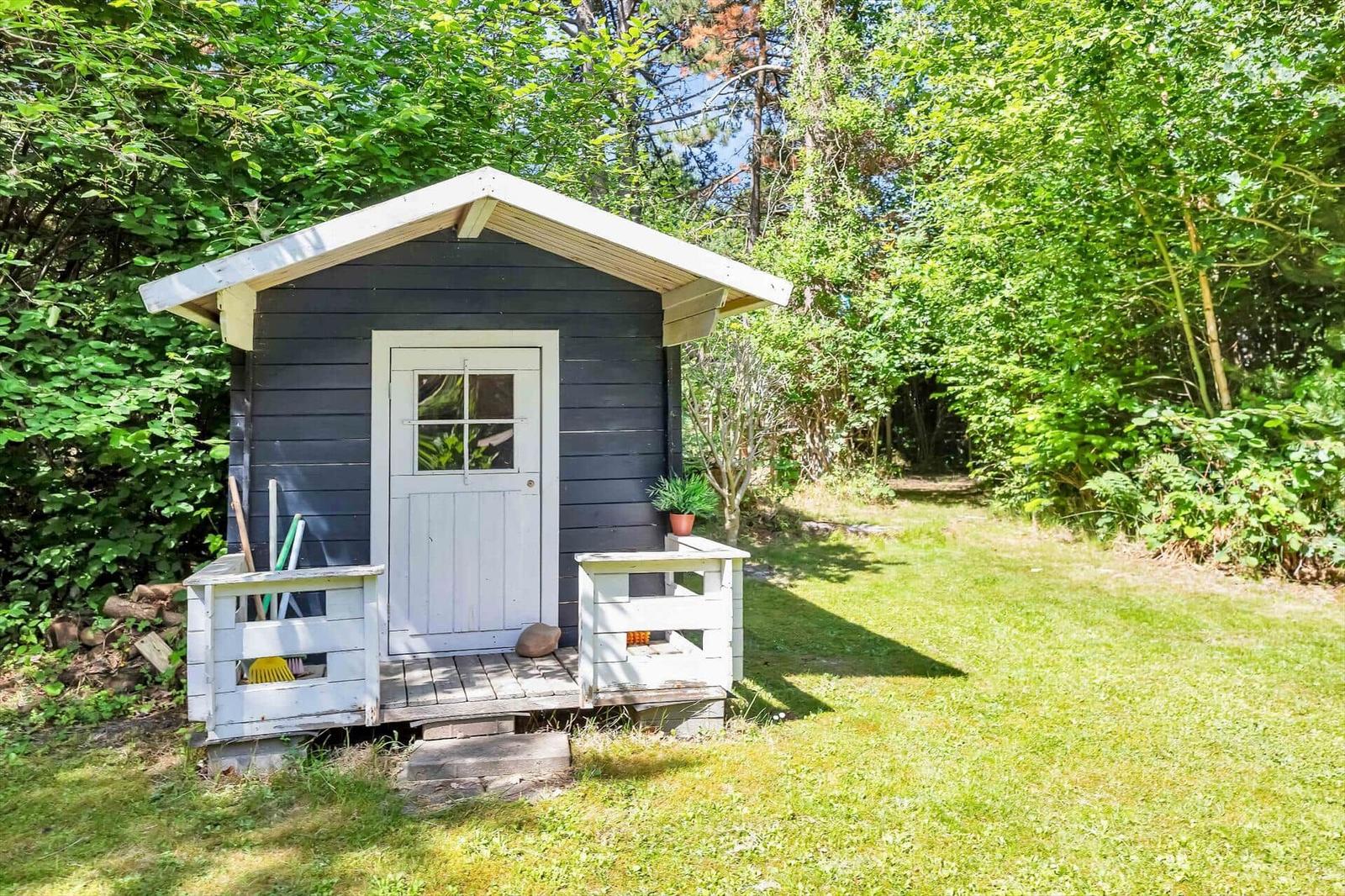 Ein kleines Holzhaus mit weißer Tür und Veranda im Grünen.