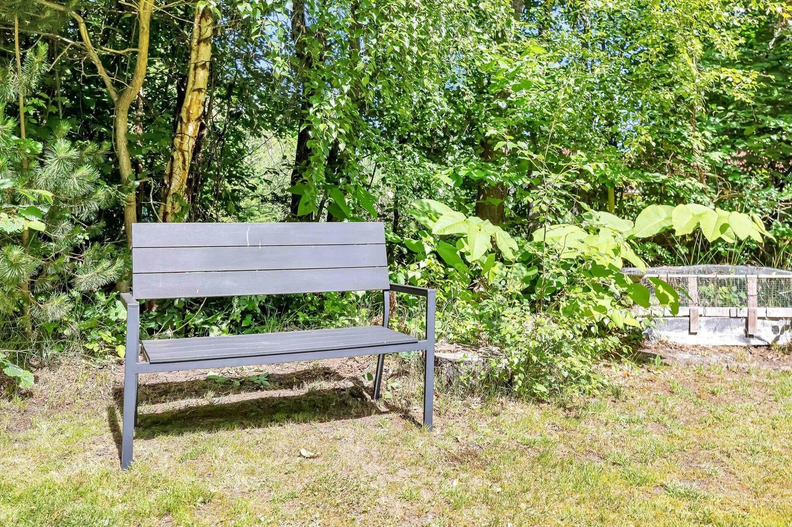 Eine graue Bank steht im Garten unter Bäumen.