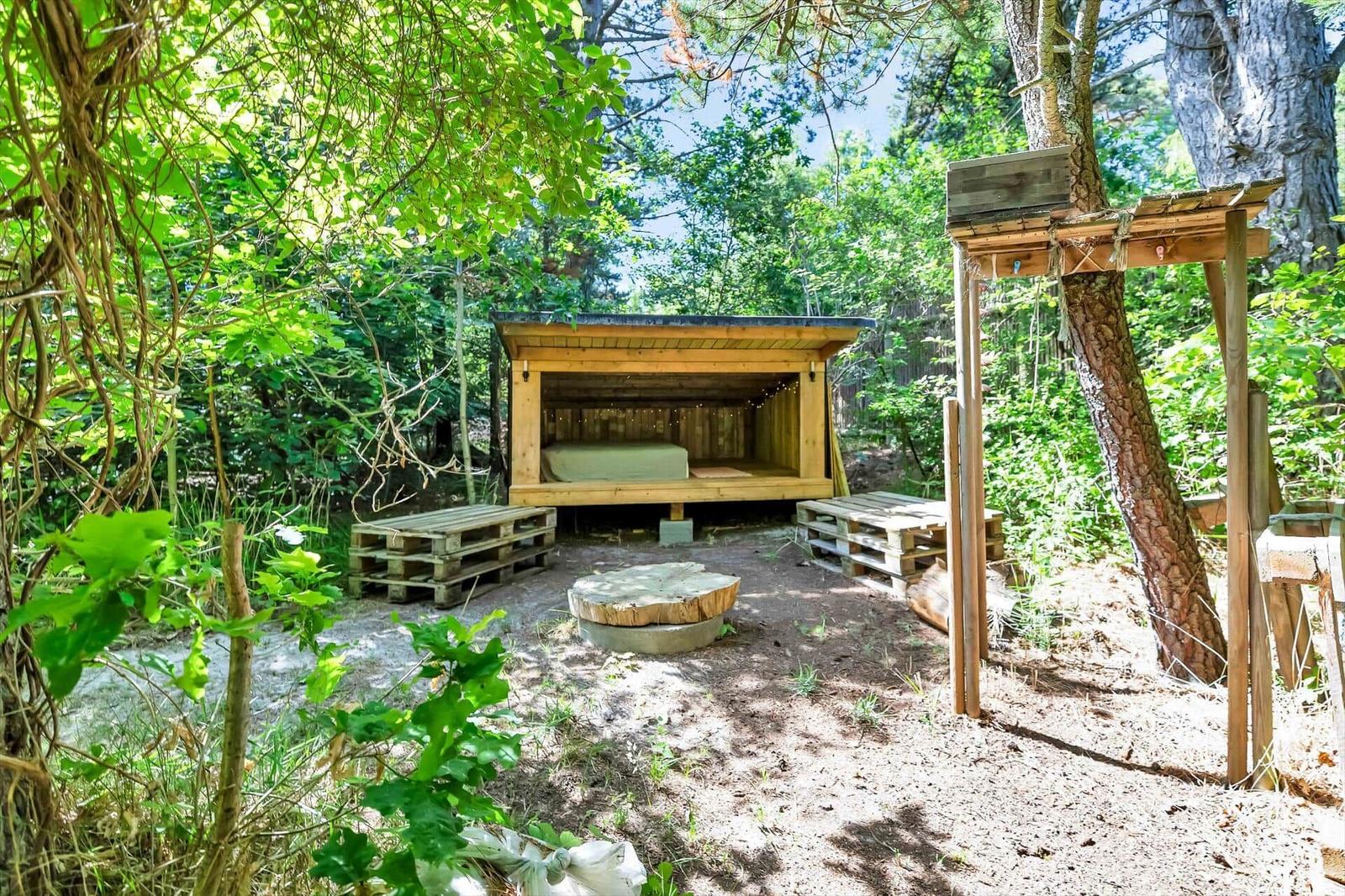 Holzkonstruktion mit Bett im Wald, umgeben von Bäumen und Pflanzen.
