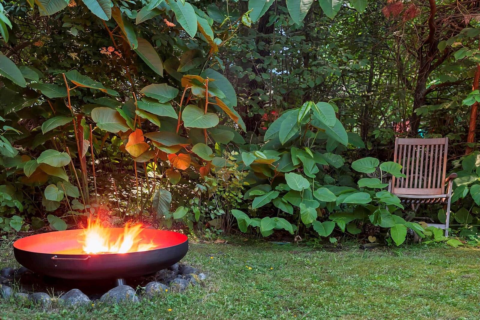 Ein brennender Feuerkessel im Garten mit Stuhl und üppiger Vegetation.