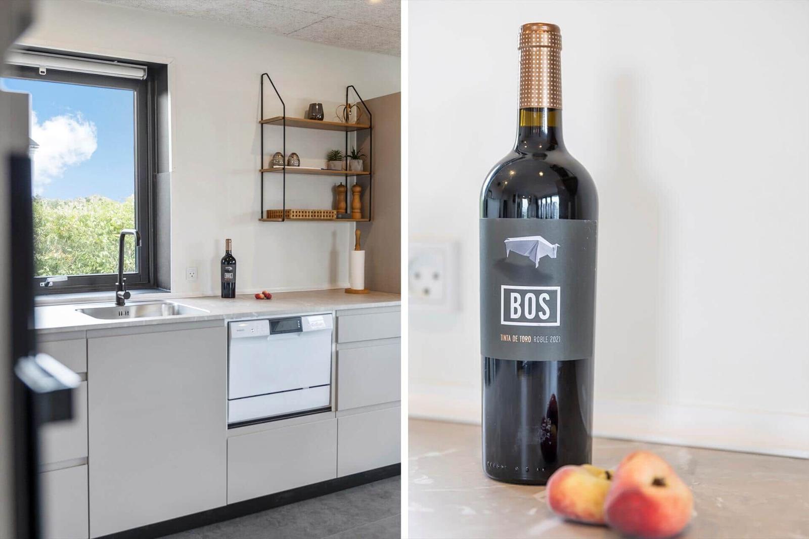 Küche mit Fenster und Waschmaschine. Flasche Wein und Pfirsiche auf Tisch.