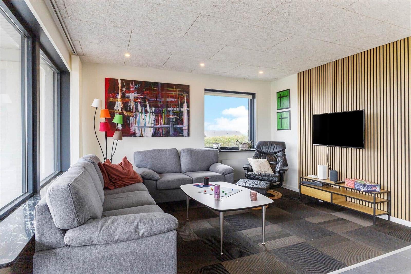 Wohnzimmer mit Sofa, Sessel und Fernseher an Holzwand
