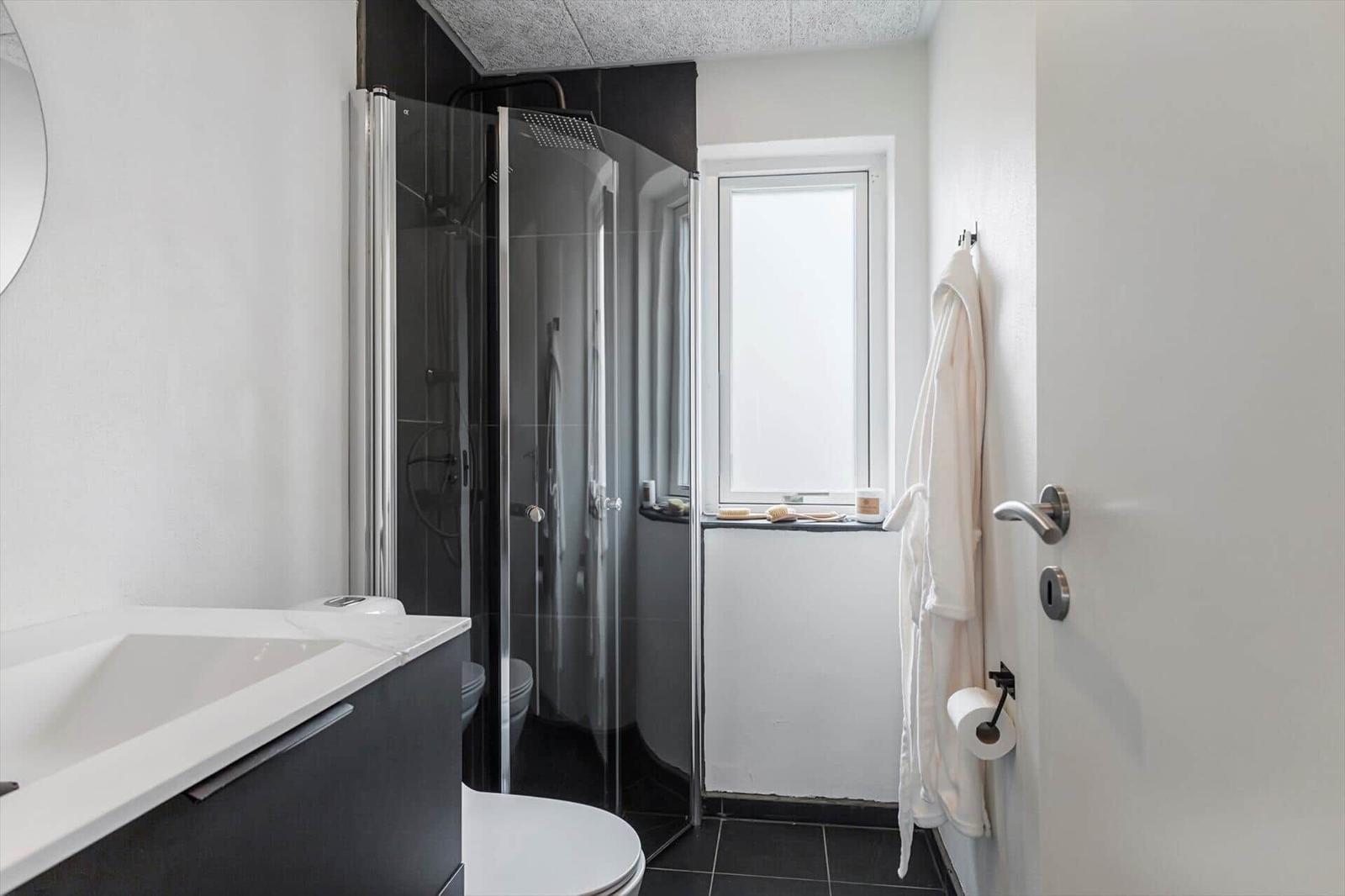 Badezimmer mit Dusche, Toilette und Waschtisch. Weiße Wände und schwarze Fliesen.