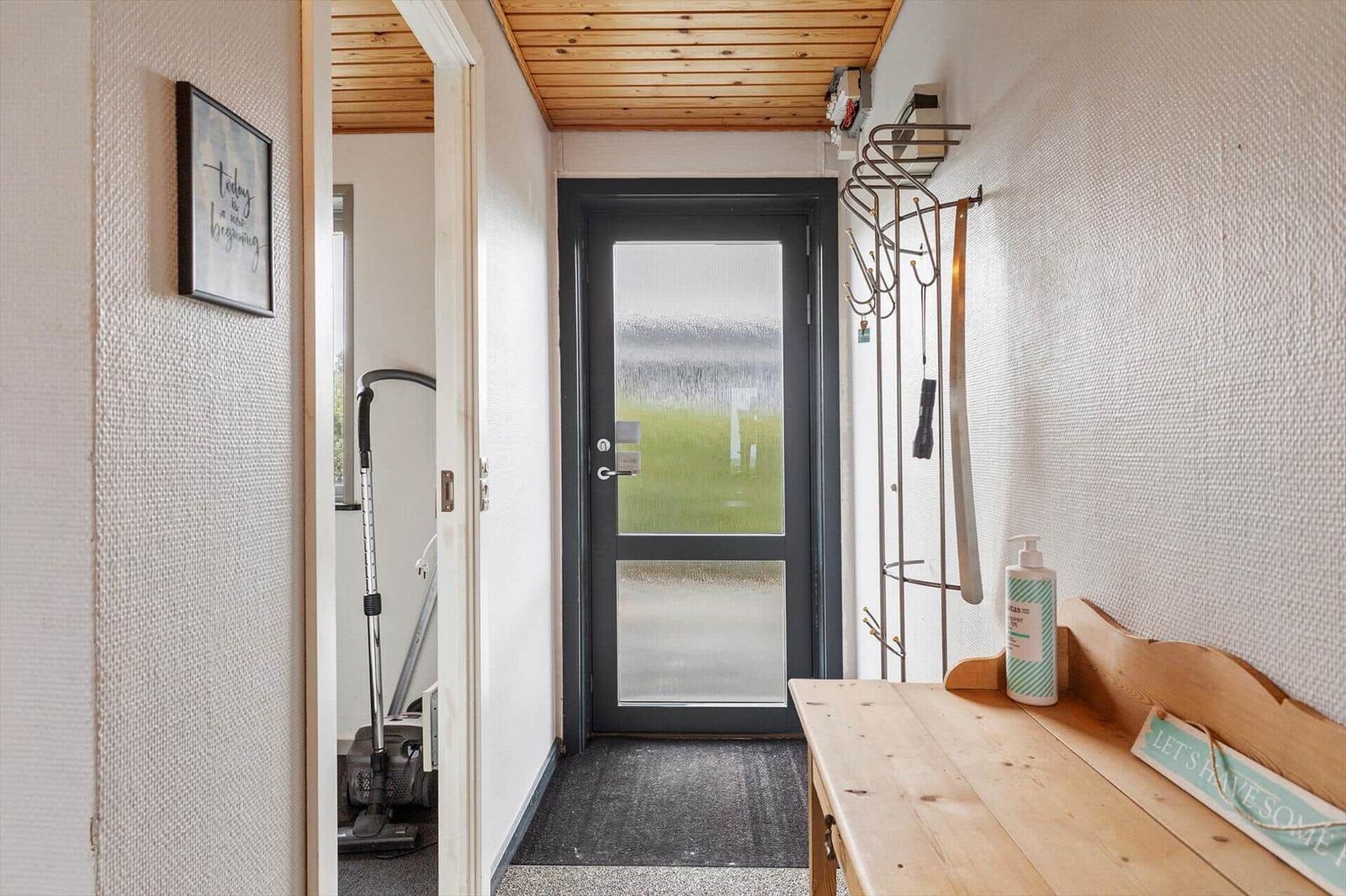 Eingangsbereich mit Holzdecke, Tür mit getöntem Glas und Holzbank mit Flasche.