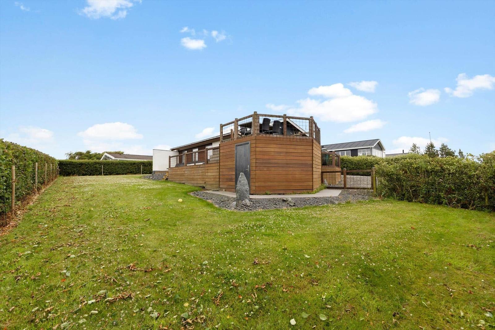 Holzhaus mit Terrasse und Garten. Himmel blau, Gras grün.