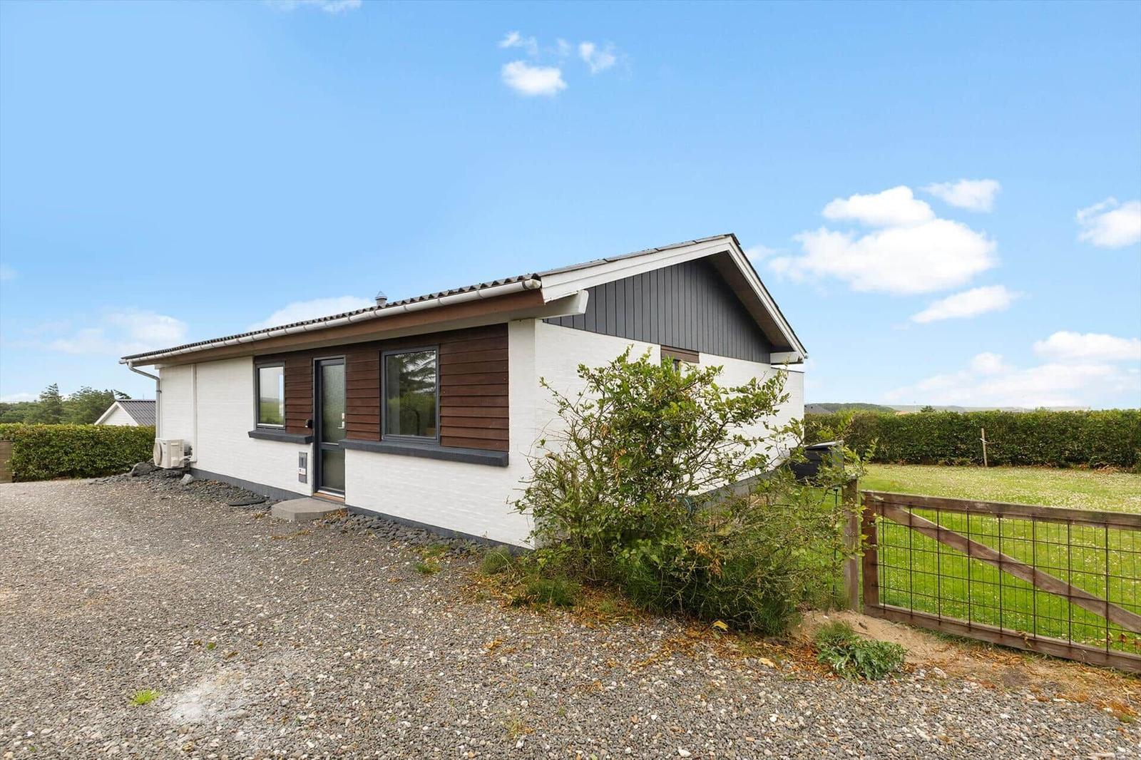 Moderne Ferienhaus mit weißen Wänden und braunen Holzverkleidungen, umgeben von Grünfläche und Zaun.
