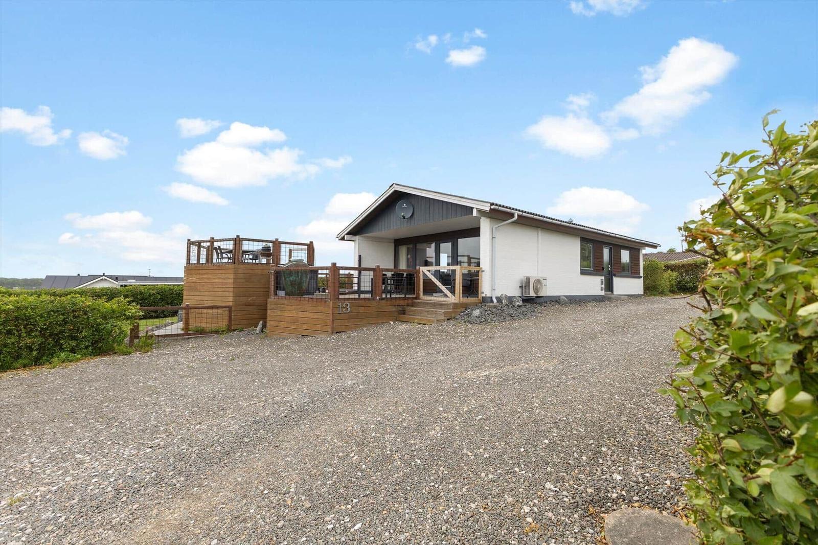 Moderne Ferienwohnung mit Holzterrasse und Garten. Kiesweg führt zum Eingang.