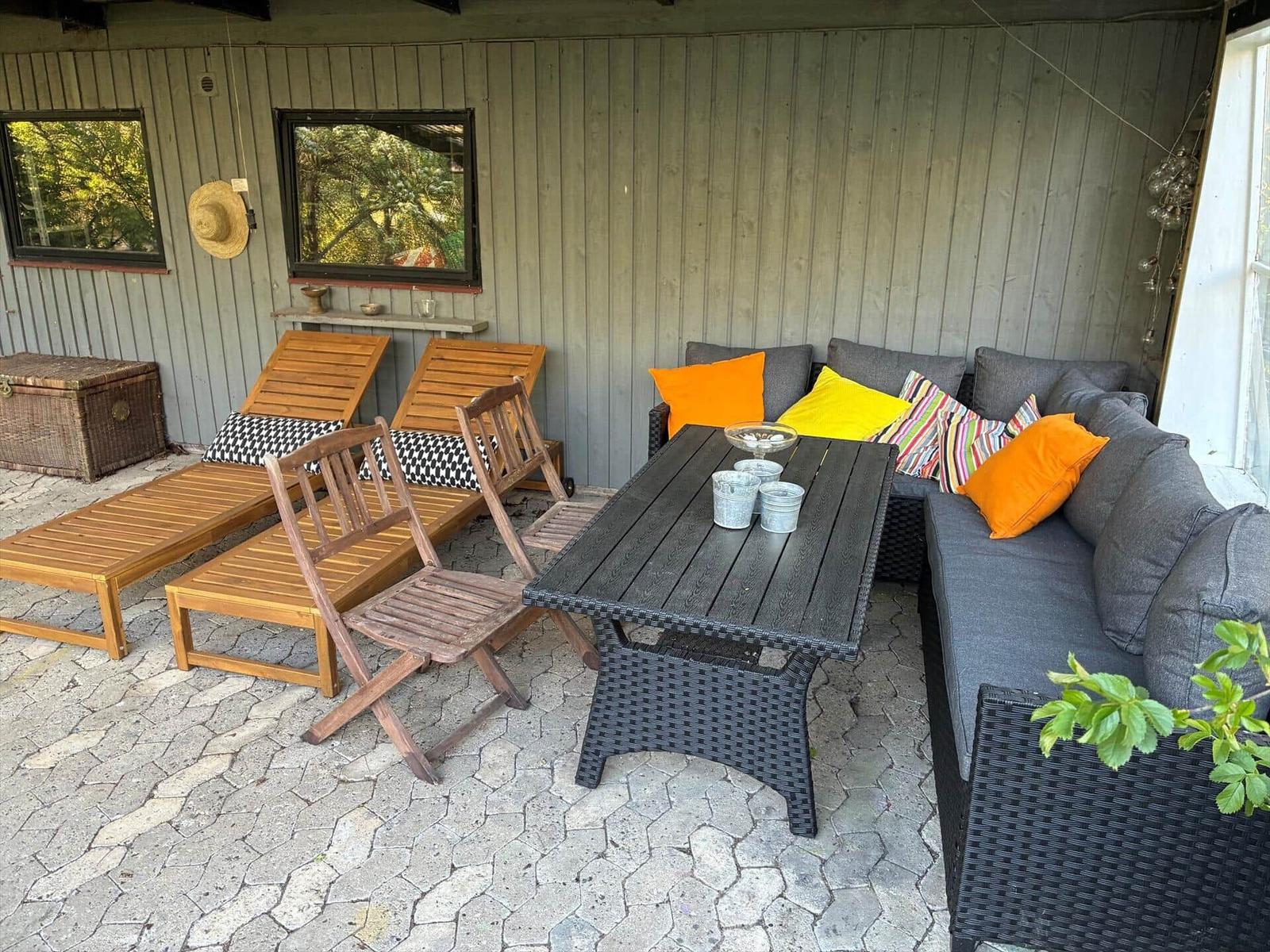 Terrace with seating group, table, and lounge chairs. Wooden and wicker furniture on stone paving.