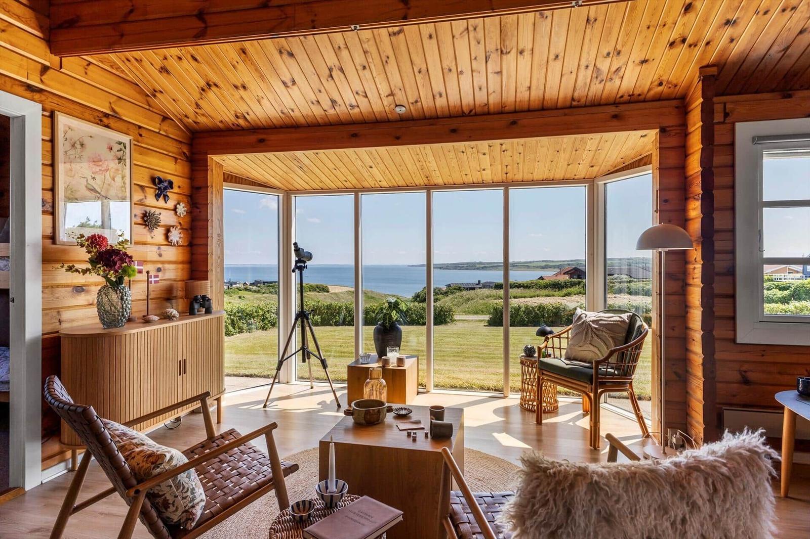 Wohnraum mit Holzwänden und großem Fensterblick auf Meer und Grünland.