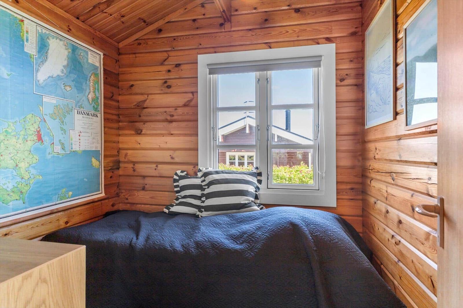 Schlafzimmer mit Holzwand, Bett, Kissen und Fenster mit Blick auf Außenbereich.