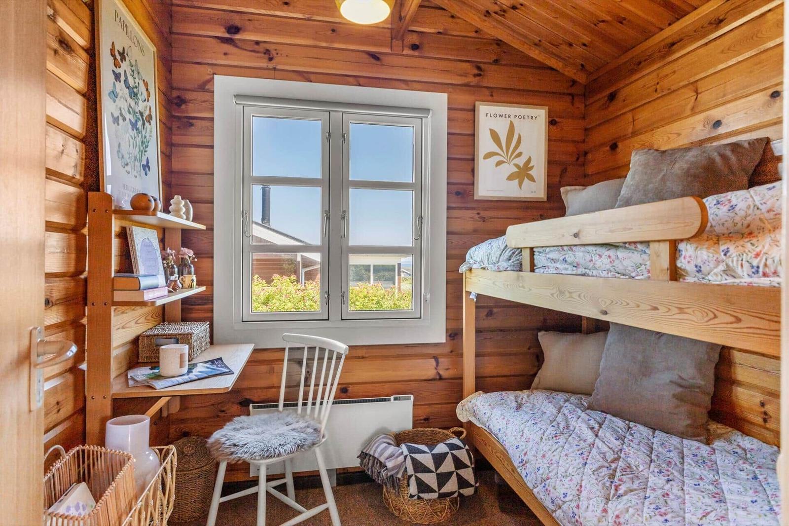 Ein Schlafzimmer mit Doppelstockbett, Schreibtisch und Fenster. Holzwände und -decke.