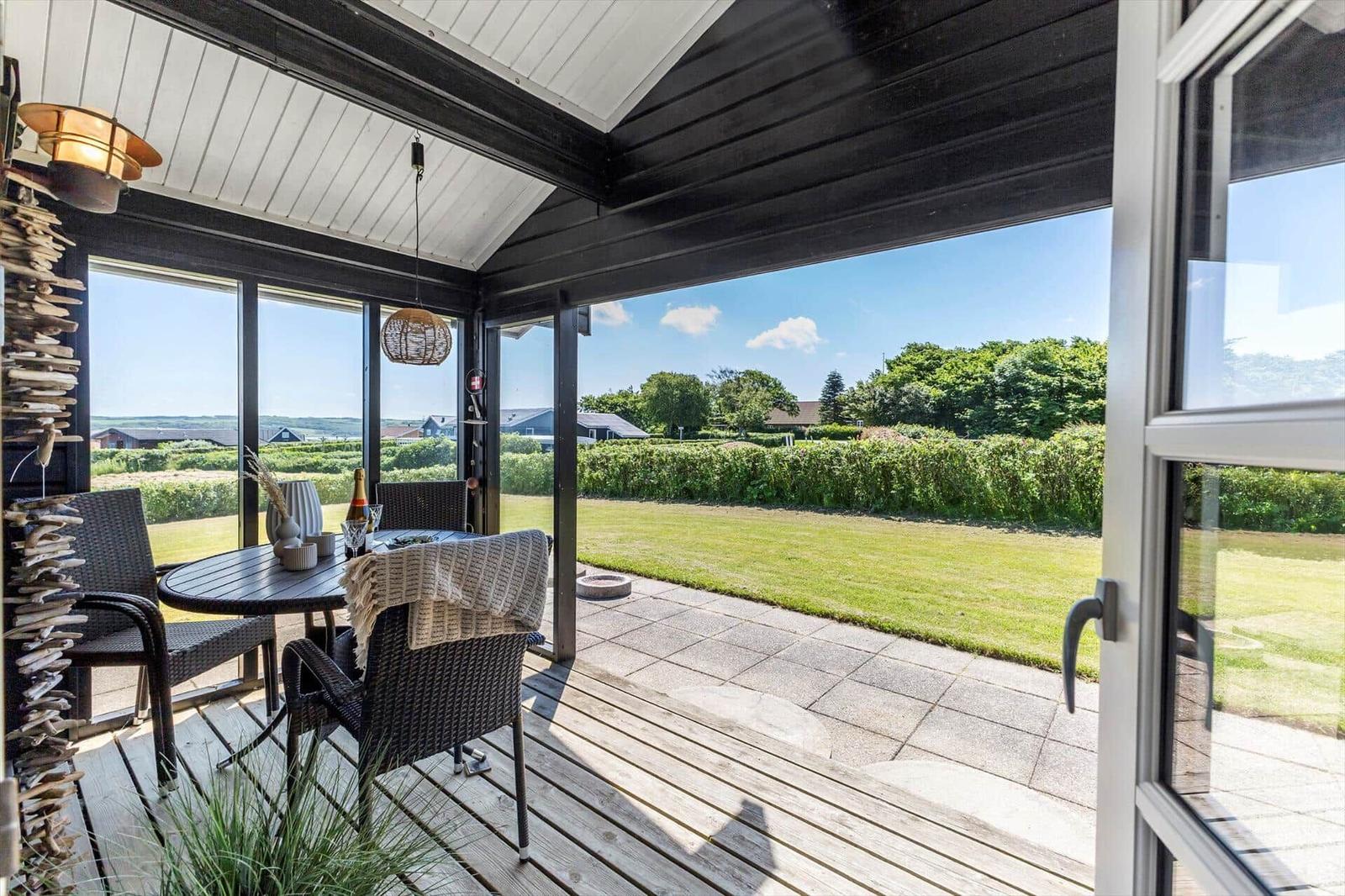 Terrasse mit Tisch, Stühlen und Blick auf grünen Rasen und Bäume.