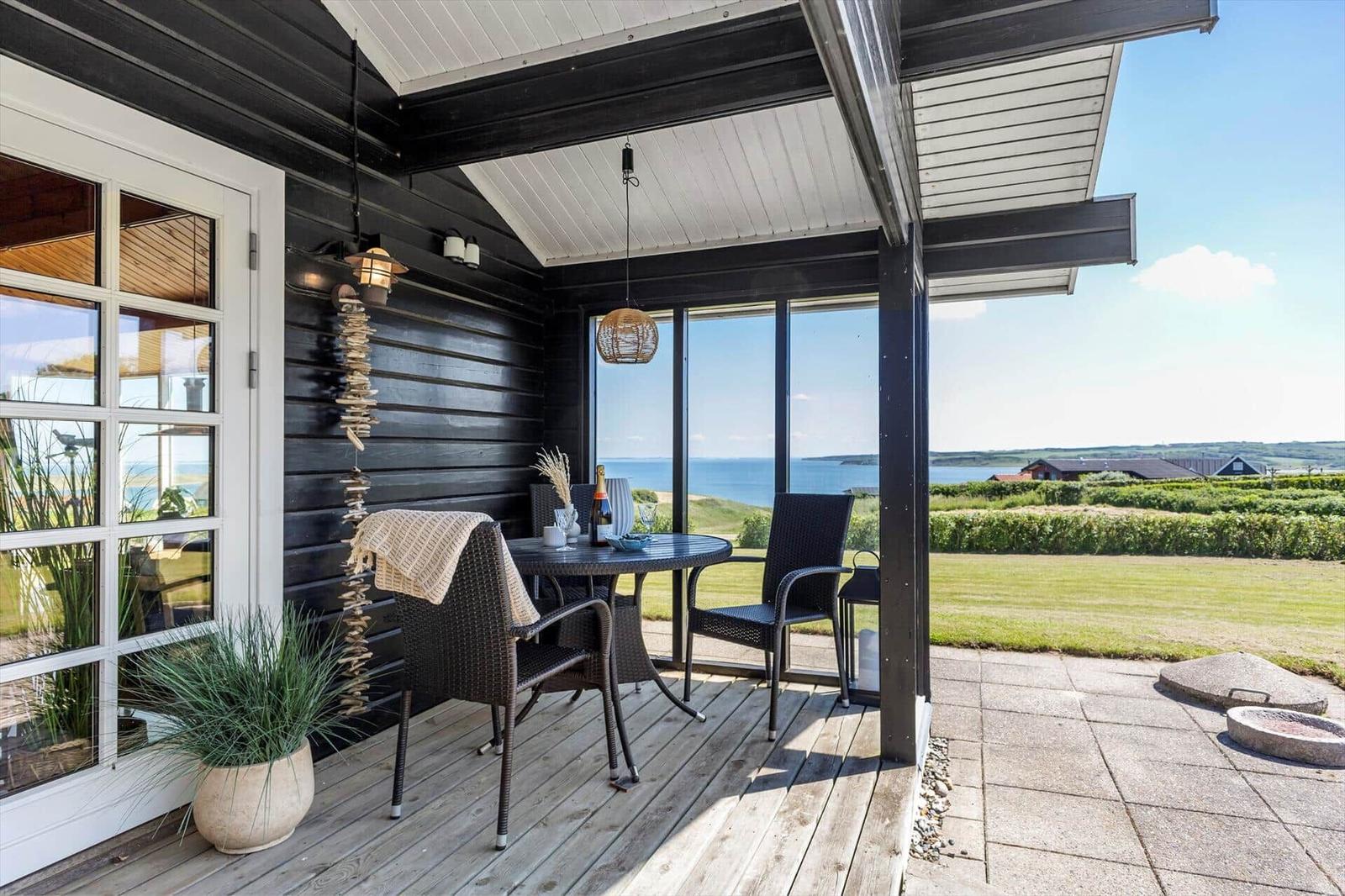 Terrasse mit Tisch und Stühlen, Blick auf Meer und Grünflächen.