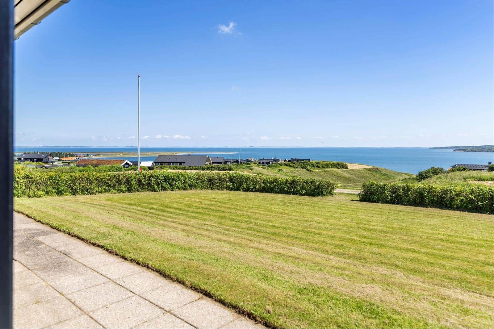 Weitläufiger Blick auf Grünflächen, Häuser und das Meer unter blauem Himmel.