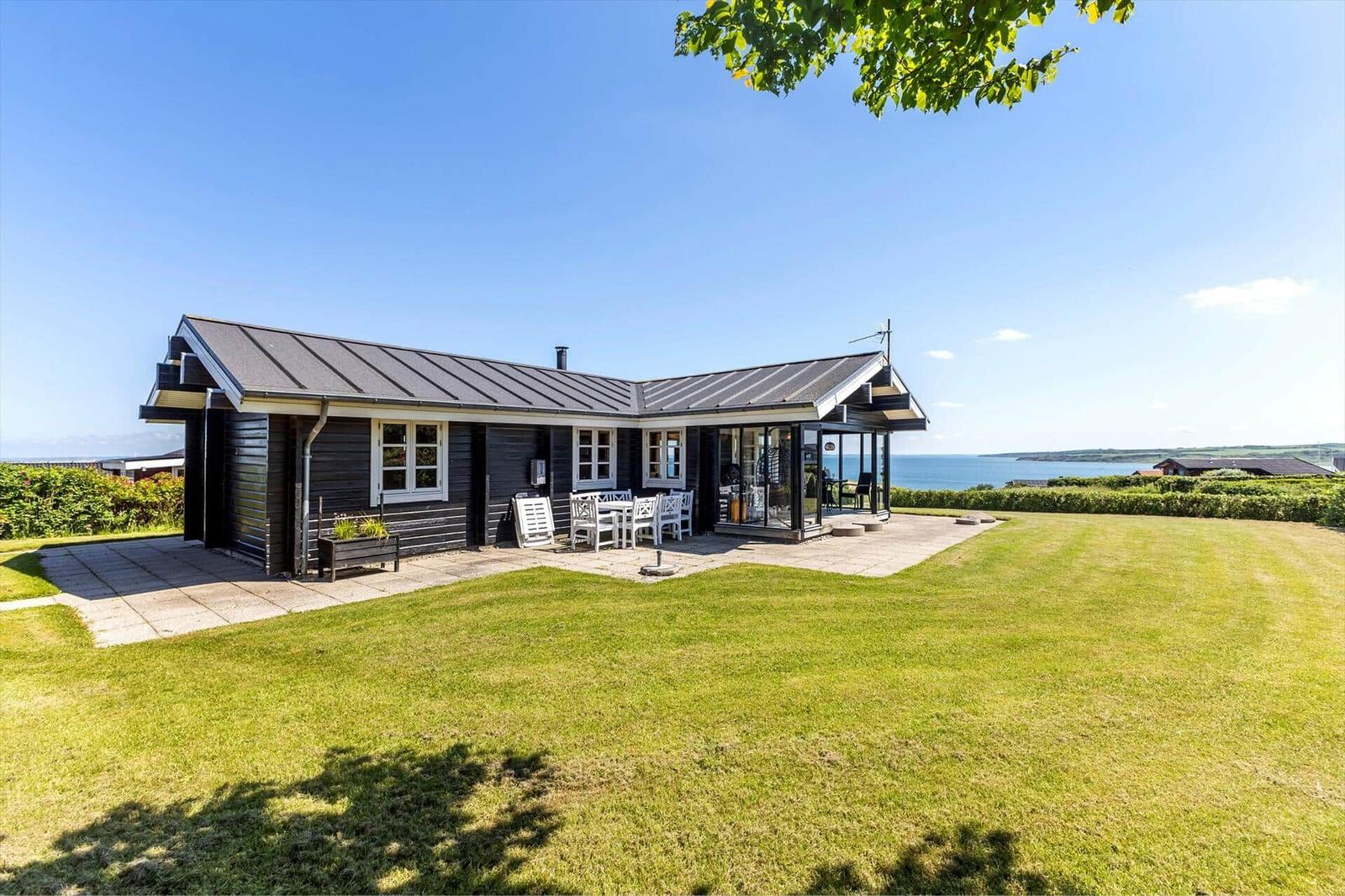 Ein Haus mit Terrasse und Blick aufs Meer. Grasfläche und Himmel sind klar.