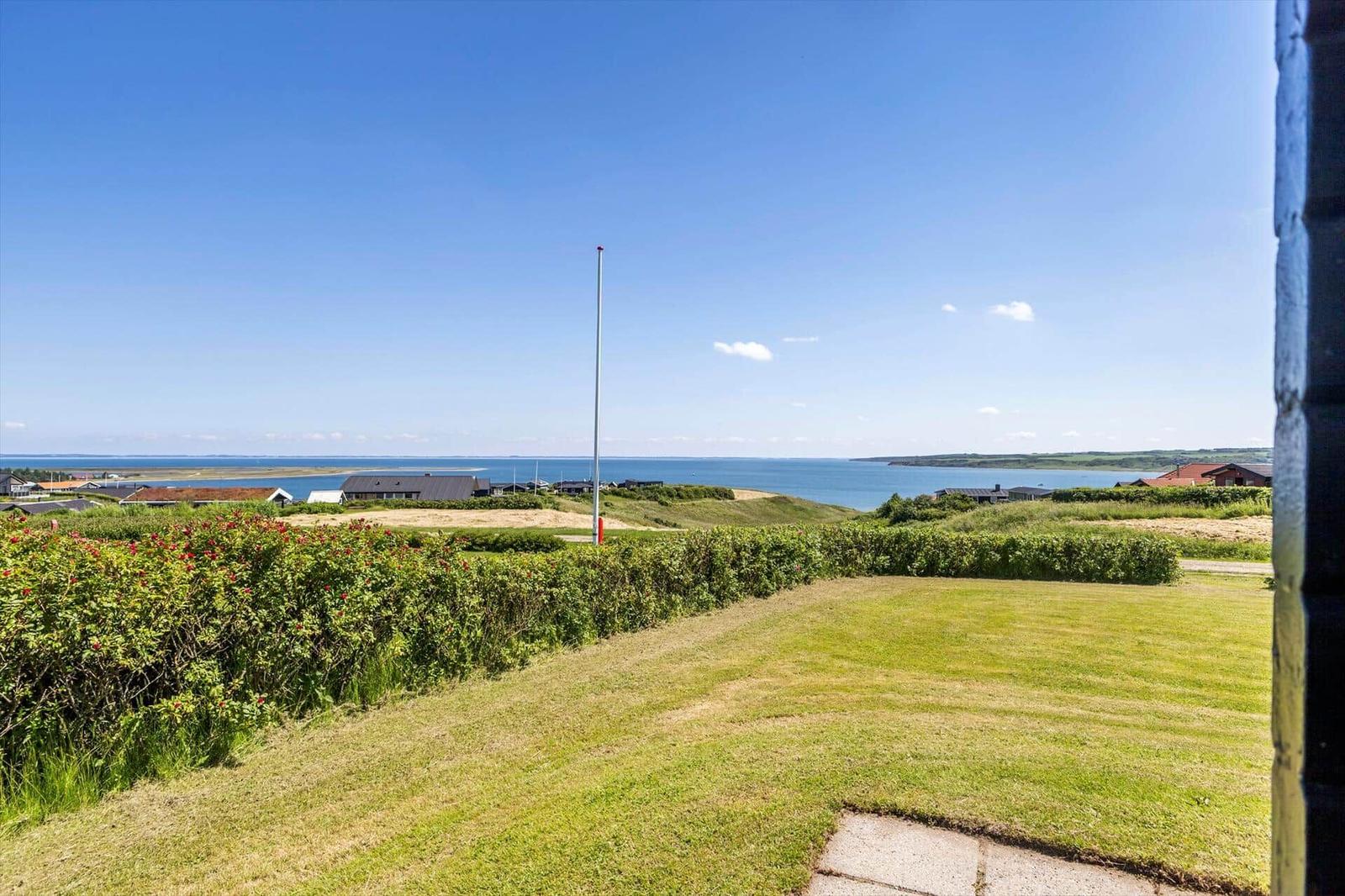 Grüner Rasenbereich mit Blick aufs Meer und einige Häuser im Hintergrund.