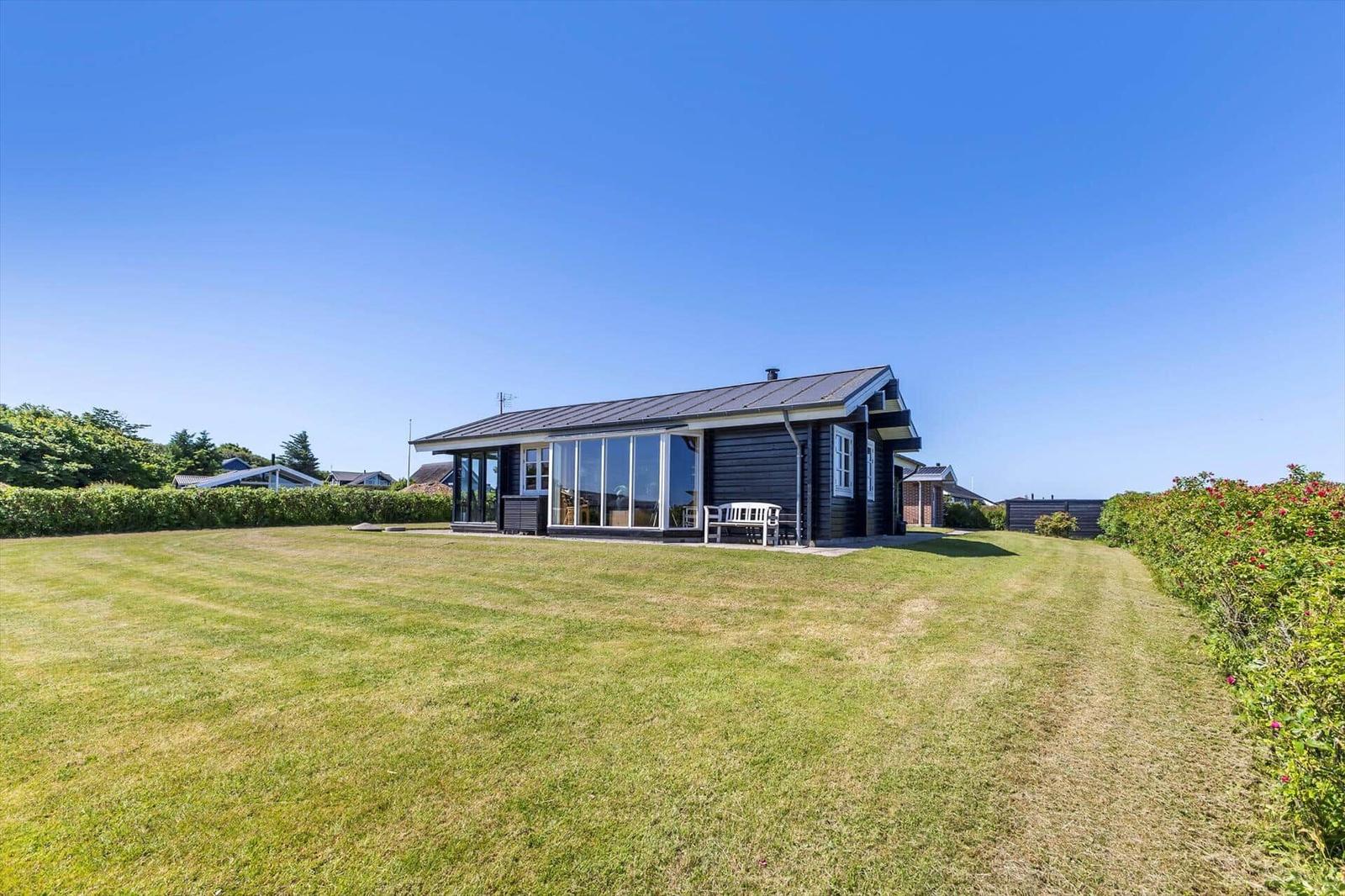 Ein schwarzes Haus mit großem Glasbereich und weißem Gartenmöbel auf grünem Rasen.