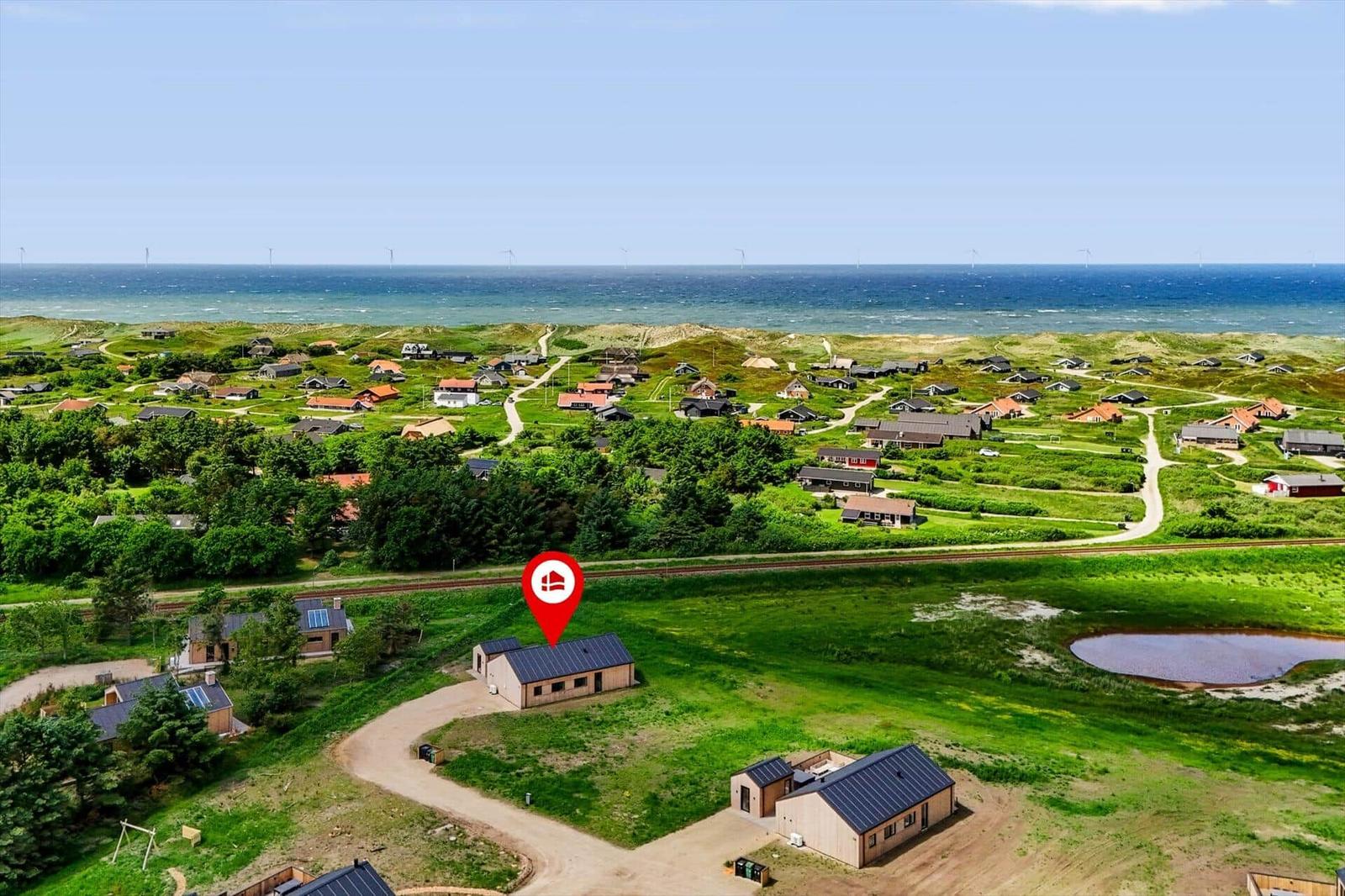 Haus mit Solaranlage in grüner Landschaft nahe Strand und Windkraftanlagen