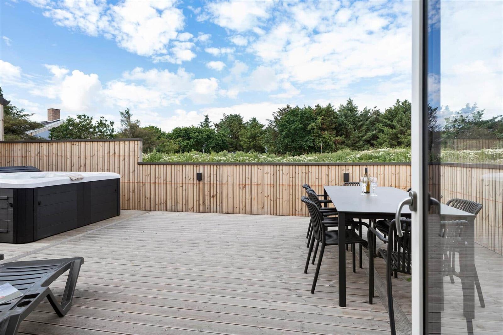 Terrasse mit Hot Tub, Esstisch und Gartenzaun unter blauem Himmel.