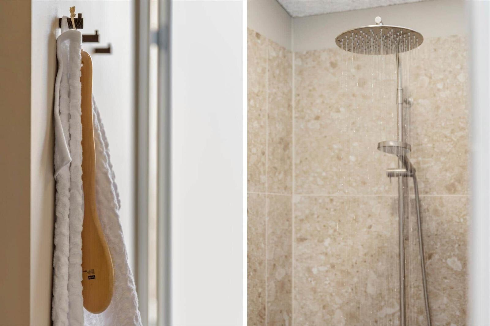 Dusche mit Regenduschkopf und Steinfliesen. Handtuch und Badezubehör hängen bereit.