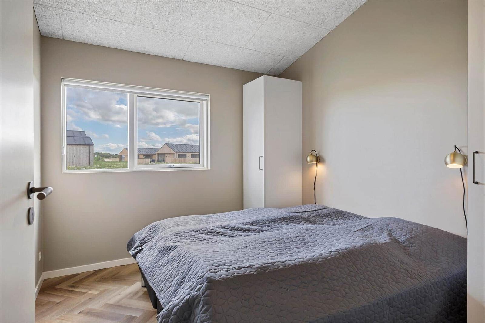 Schlafzimmer mit Bett, Fenster und Kleiderschrank. Holzboden und Wandlampen.