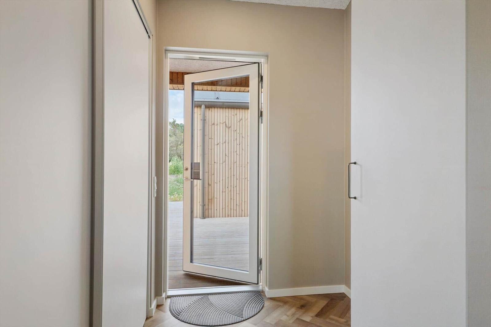 Eingang mit geöffneter Glastür zum Außenbereich mit Holzdecke und Holzwand.