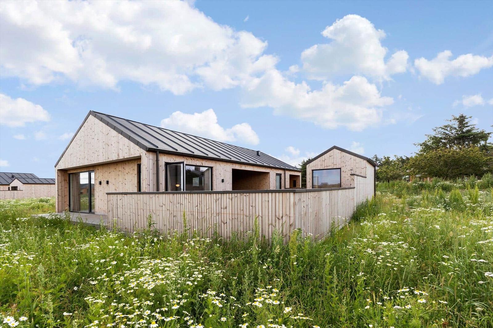 Moderne Holzhütte mit großem Balkon und Gartenterrasse im Gras mit Blumen.