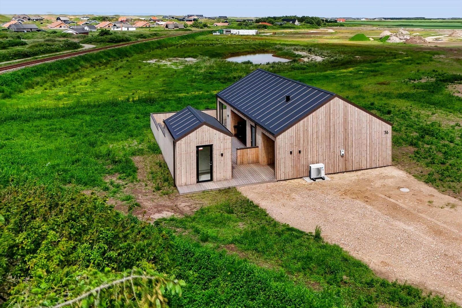 Moderne Holzhütte mit schwarzem Dach in grüner Landschaft.