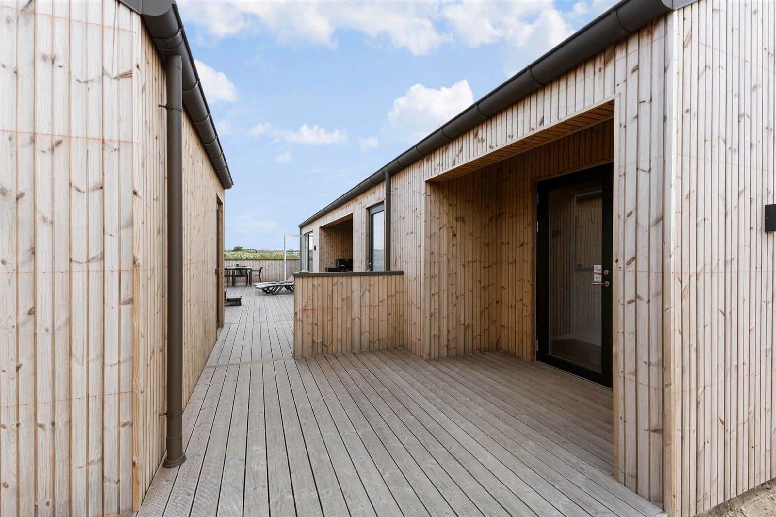 Holzveranda mit Außentür und Sicht auf Terrasse mit Tisch und Liegen.